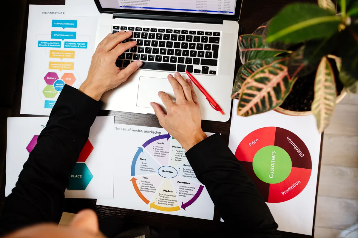 Hands working on a laptop surrounded by planning charts
